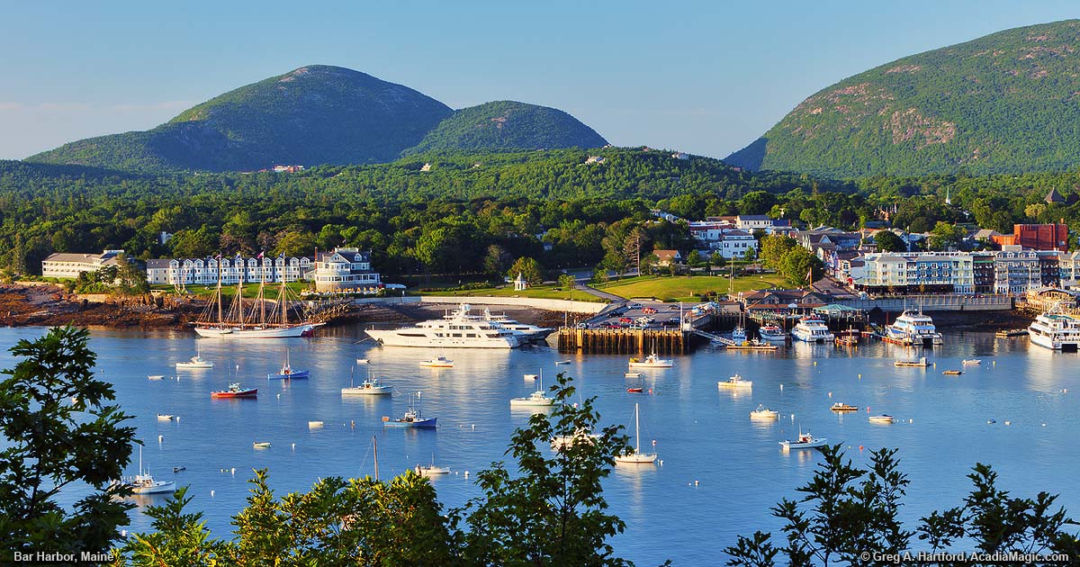 Scenic view of Bar Harbor’s waterfront with docked boats, coastal buildings, and forested mountains in the background, capturing the town’s blend of natural beauty and small-town charm.