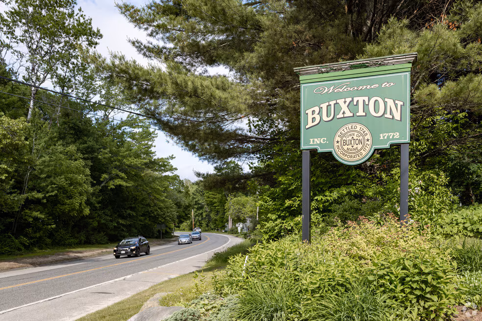 Welcome sign at the roadside entrance to Buxton, Maine surrounded by trees and greenery.