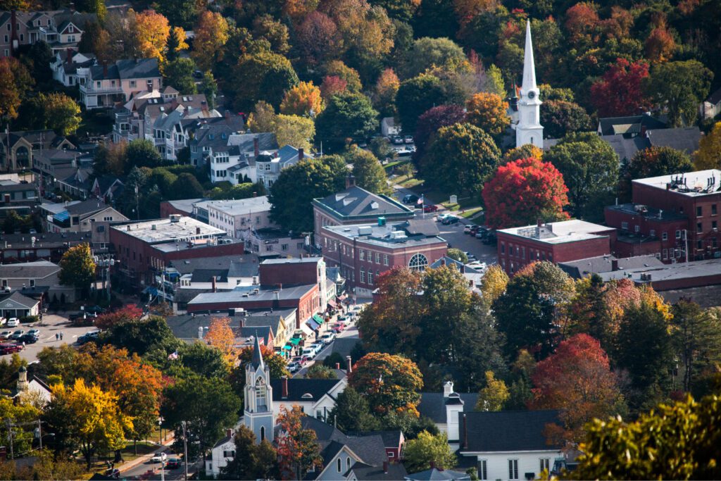 Aerial view of downtown Camden, Maine in autumn, with colorful trees surrounding historic brick buildings and coastal streets leading toward the harbor.