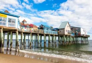 View of Cape Elizabeth pier with colorful seaside buildings and reflections on the water, under a partly cloudy sky.