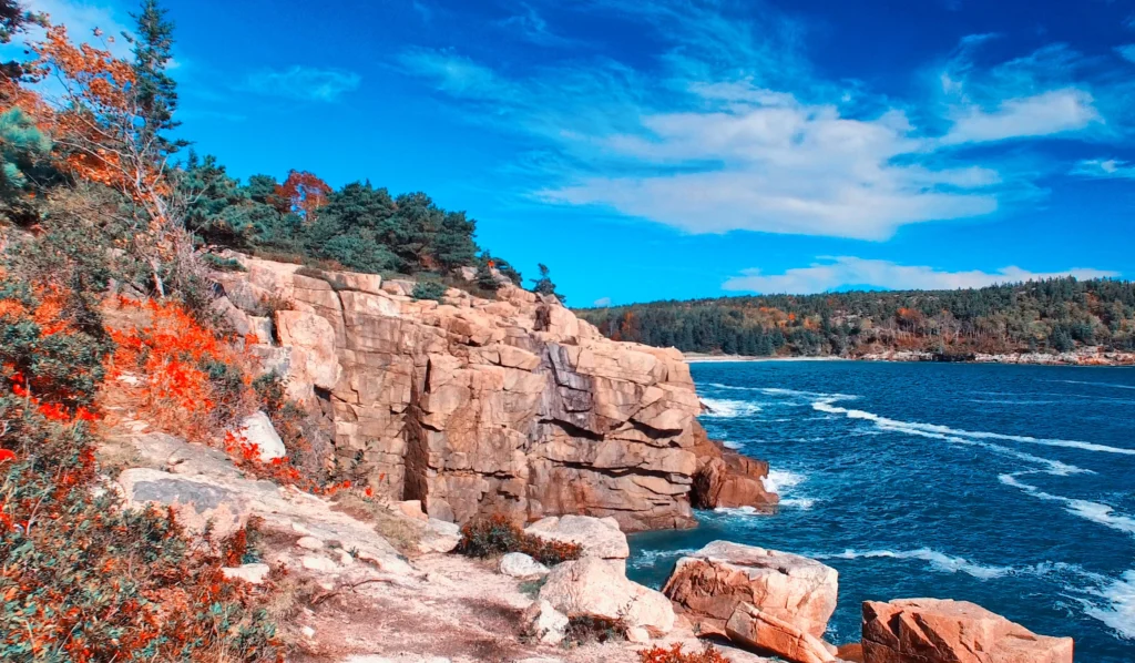 Rocky coastline and blue waters in Caribou, Maine, framed by evergreens and a bright sky on a crisp day.