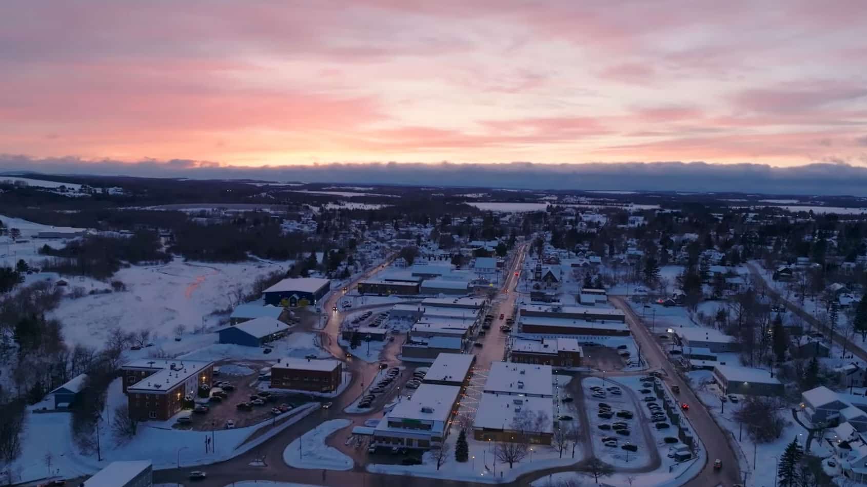 A winter sunrise over Caribou, Maine, showing rooftops dusted with snow and a soft pink sky above the quiet northern town.