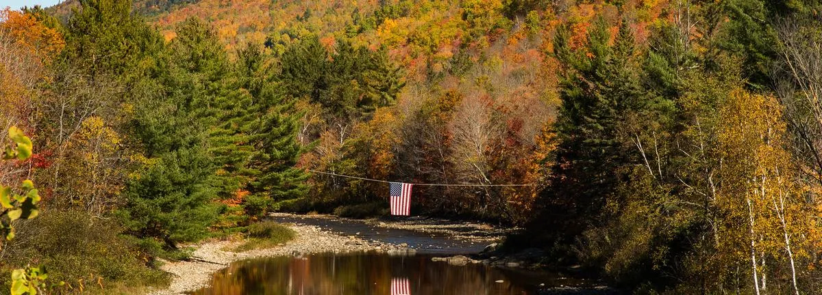 Scenic autumn landscape in Carrabassett Valley with American flag over a quiet river, symbolizing the town’s seasonal rhythm and the role of managed IT in supporting rural connectivity.