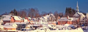 Scenic view of downtown Damariscotta, Maine in winter, featuring historic waterfront buildings, snow-covered rooftops, and a peaceful harbor setting.