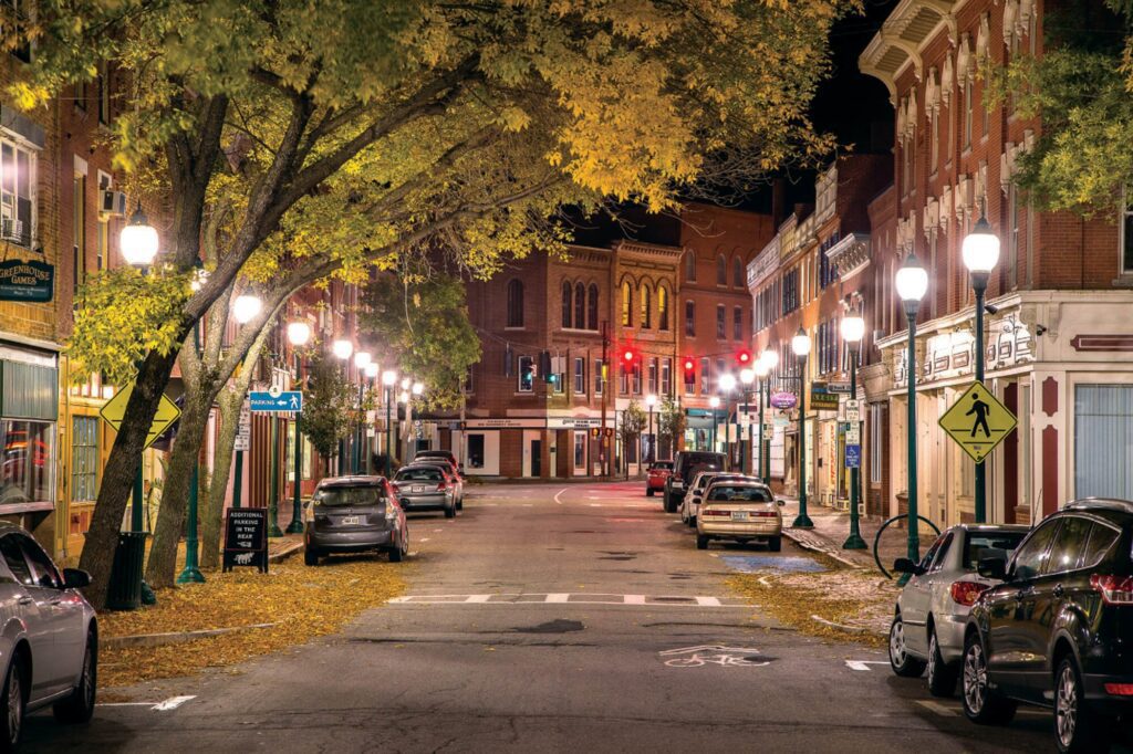 Water Street in downtown Gardiner, Maine at night, lit by streetlamps with parked cars and historic brick buildings lining the street.