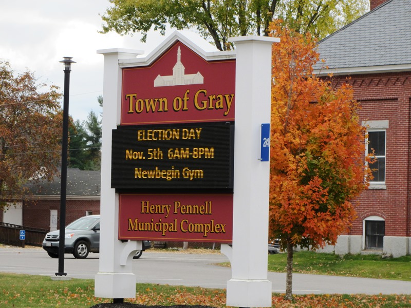 Election announcement sign for the Town of Gray, located at the Henry Pennell Municipal Complex, with fall foliage and a brick building in the background.