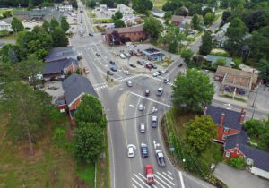 Aerial view of downtown Gray, Maine, showing intersecting roads, surrounding shops, and tree-lined residential areas on a summer day.