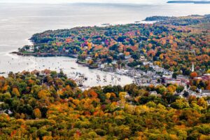 Scenic aerial view of Hampden, Maine in peak autumn, overlooking the Penobscot River with vibrant fall foliage and waterfront homes.