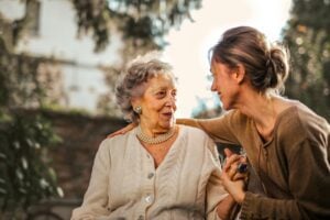 Elderly woman and caregiver sharing a moment outdoors, illustrating compassionate tech support for senior care.