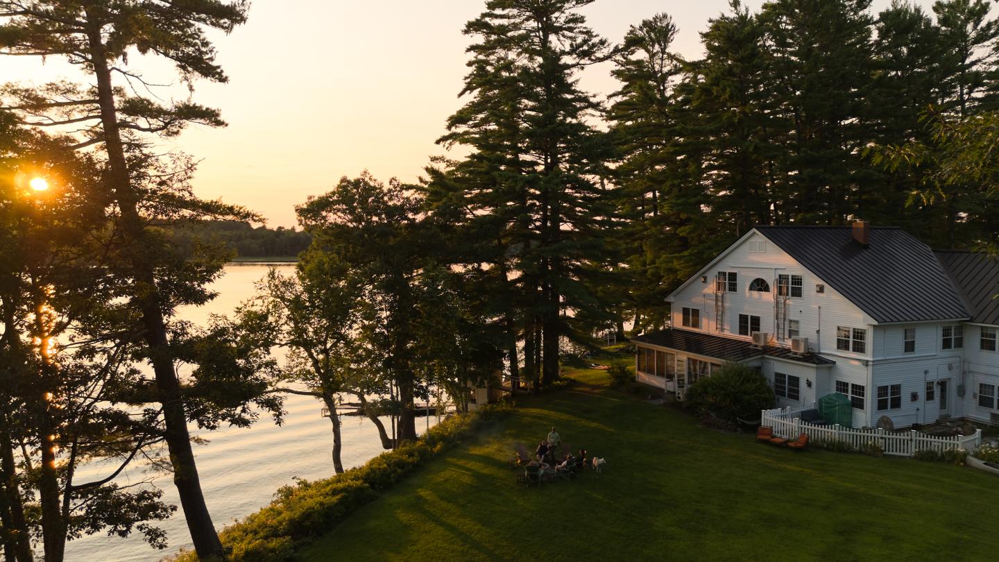 Sunset view of a lakeside building surrounded by tall pines in Poland, Maine—representing the calm reliability and scenic backdrop that managed IT services help protect and support.