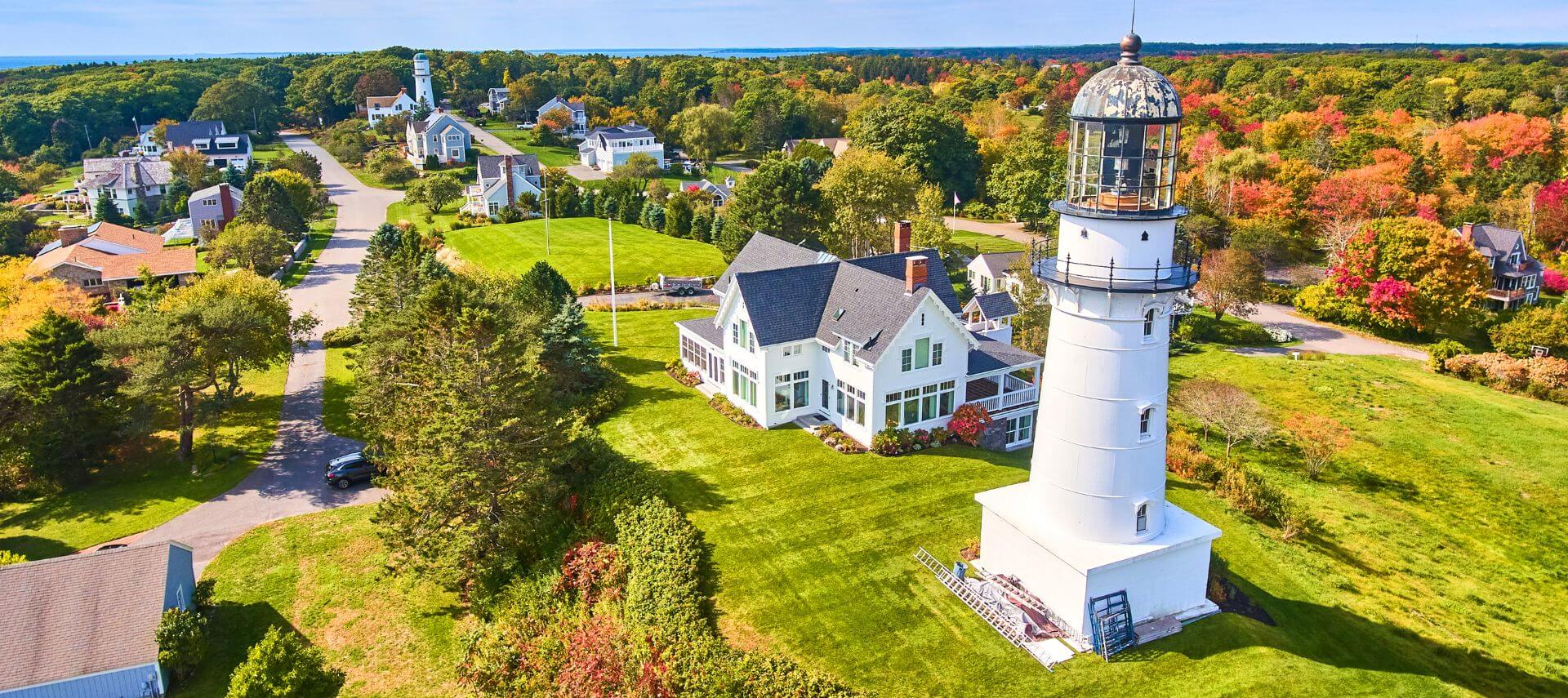 Overhead view of a coastal Maine lighthouse surrounded by fall foliage and homes, reflecting the stability and community support behind local managed IT services.